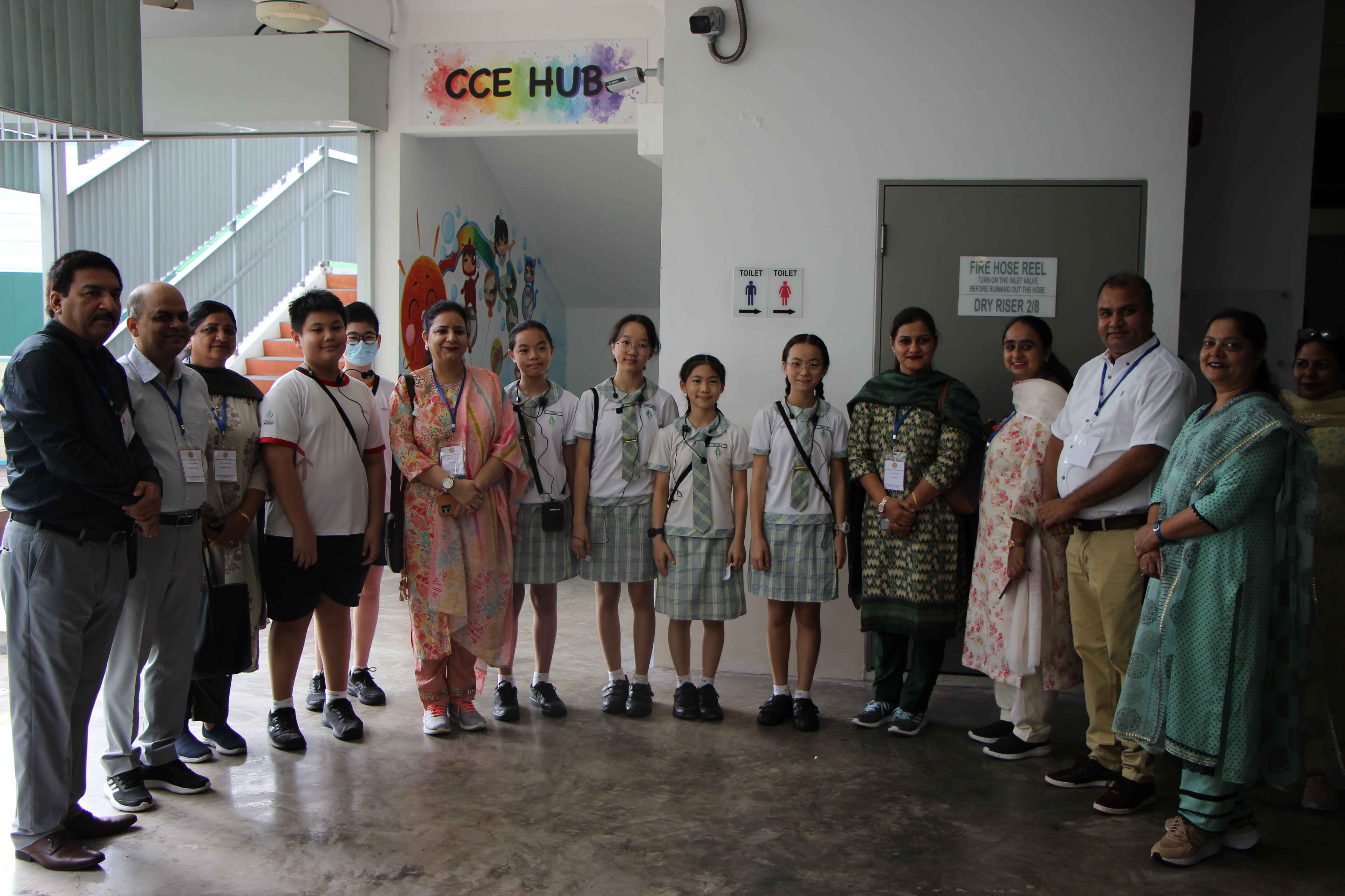 A group of students in uniforms and adults standing together indoors near a colorful CCE HUB sign.